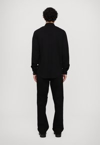 Camisa negra de manga larga con diseño de yugo curvado, puños con botón y dobladillo redondeado, combinada con pantalones negros a juego.