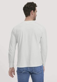 Wit katoenen t-shirt met lange mouwen, gezien vanaf de achterkant, met een ronde halslijn en ribbenboorden, gecombineerd met blauwe denim jeans.