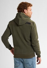 Olijfgroene hoodie van een textuur fleece-materiaal, voorzien van een capuchon met trekkoord en een contrasterende donkere vlek op de bovenrug.
