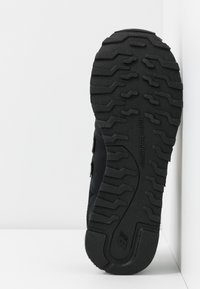 Svart skosula med texturerat mönster för grepp, med en dämpad design och varumärke präntat på sidan. Slät och gummiartad yta.