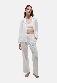 Ensemble de vêtements d'intérieur blanc composé d'une chemise à boutons avec poches et d'un pantalon à coupe décontractée, présentant une texture lisse et un design minimaliste.