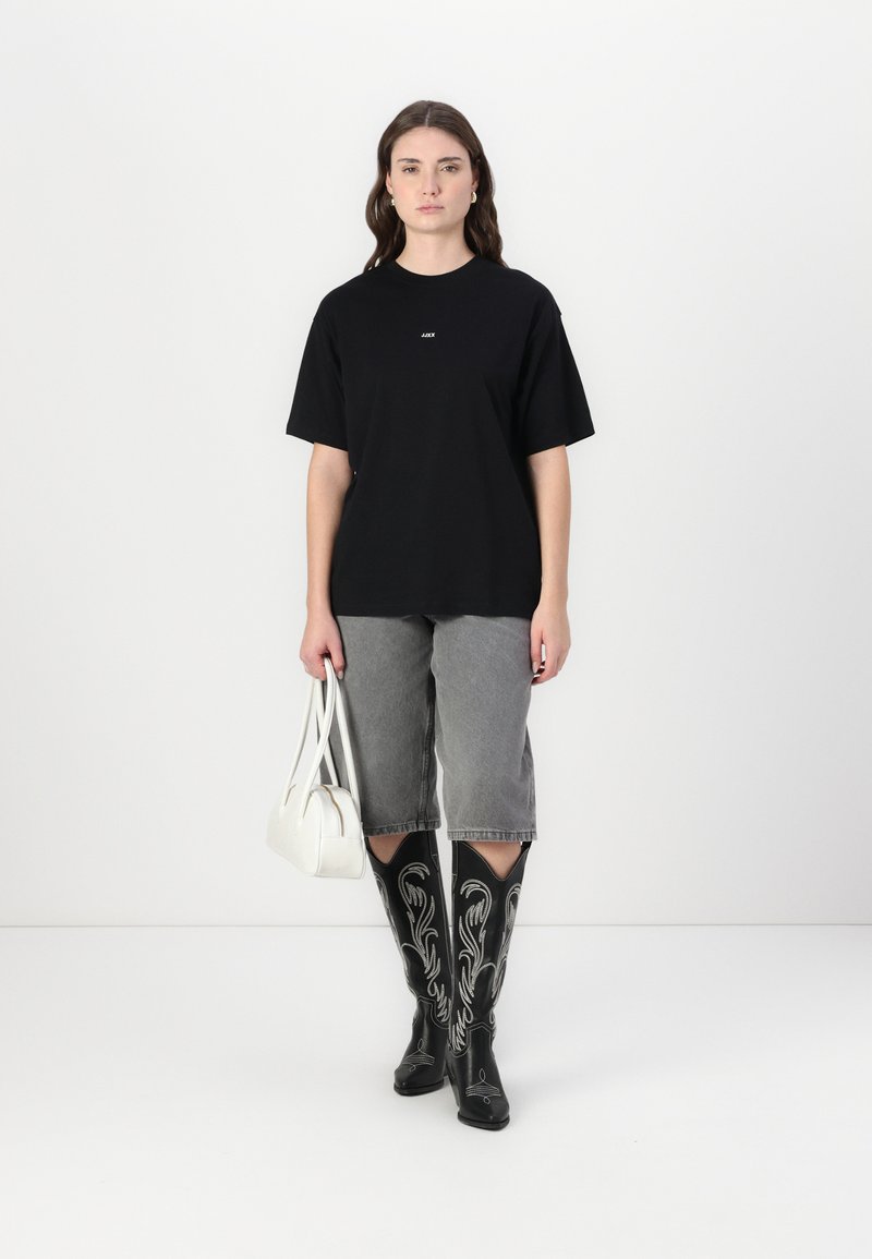 Black oversized t-shirt, gray denim shorts, black embroidered knee-high boots, white handbag. Model stands against a plain background.