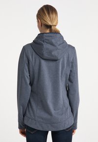 Veste grise à capuche en tissu doux et texturé. Caractérisée par une coupe décontractée, des manches longues et un ourlet incurvé. Design minimaliste sans logo visible.