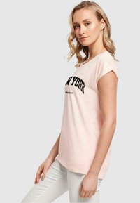 Heled roosa lühikeste sleeves'iga T-särk ümara kaelusega, millel on rinnal bold must "NEW YORK" tekst sportlikus fondis.