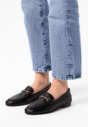 Zwarte leren loafers met een gouden kettingdetail, platte zool en ronde neus. Draag met lichtblauwe cropped denim jeans.
