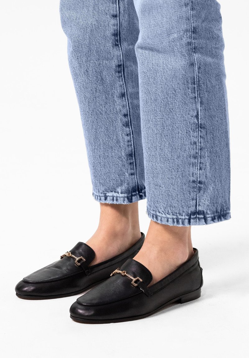 Zwarte leren loafers met een gouden kettingdetail, platte zool en ronde neus. Draag met lichtblauwe cropped denim jeans.
