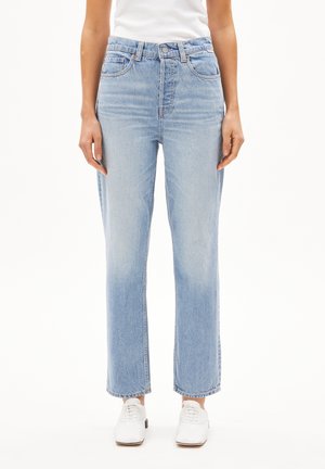 Front view of a person wearing light blue straight-leg jeans, white sneakers, and a white top, standing with arms relaxed at sides.