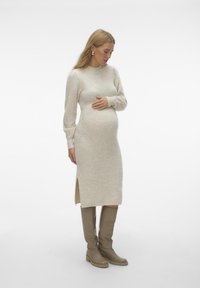 Abito premaman beige in maglia con maniche lunghe e spacchi laterali, abbinato a stivali beige fino al ginocchio, texture liscia, design minimalista.