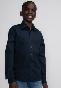 Navy button-up shirt met lange mouwen, kraagontwerp en gestikte accenten, gecombineerd met blauwe denim jeans. Uniform stof textuur.