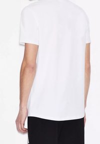 Vit kortärmad t-shirt med rund halsringning, slät textur och rak fåll, sedd bakifrån mot en neutral bakgrund.