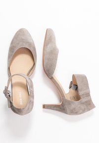 Harmaan mokkasiinimaiset korkokengät, joissa on pyöreä kärki ja nilkkaremmi. Ominaisuuksina matala leikkaus ja sileä nahkamainen pohja.