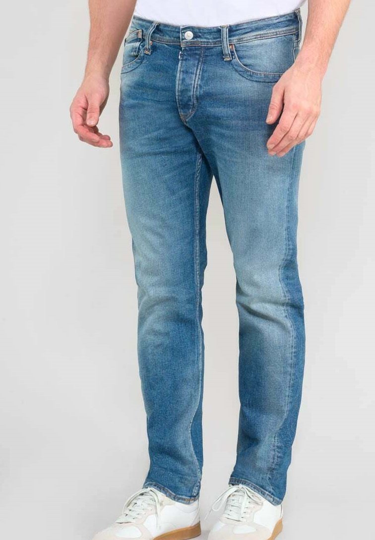 Jean en denim bleu clair avec une coupe slim, des détails délavés, un design classique à cinq poches et une fermeture à bouton métallique, associés à des baskets blanches.