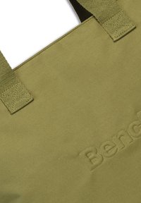 Olijfgroene schoudertas gemaakt van zacht materiaal met reliëfbranding. Beschikt over stevige, platte schouderbanden en een eenvoudig, getextureerd ontwerp.