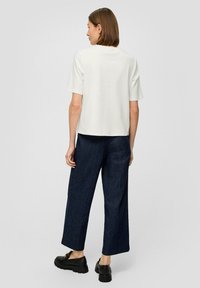 Biała bluzka krótkim rękawem w połączeniu z ciemnoniebieskimi szerokimi spodniami, charakteryzującymi się luźnym krojem i minimalistycznym designem. Czarne masywne buty dopełniają całość.