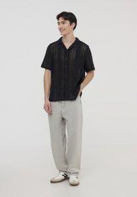 Maglietta nera a maglia aperta con maniche corte e colletto, abbinata a pantaloni grigi chiari svasati e sneakers bianche. Chiusura con bottoni semplice.