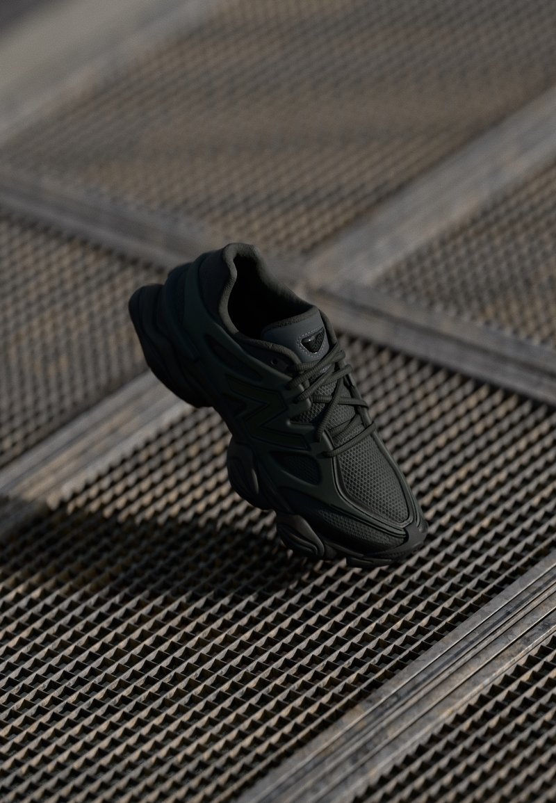 Baskets noires de sport avec mesh et superpositions synthétiques posées sur une surface métallique texturée sous un éclairage doux.