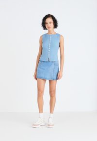 Top fără mâneci, de culoare albastru deschis, cu dungi, cu nasturi în față și un mic decolteu. Asortat cu o fustă mini din denim deschis și adidași albi cu accente.