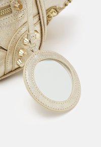 Złota torba z faux skórki z okrągłym, teksturowanym lusterkiem, ozdobiona metalowymi ćwiekami i detalem w postaci zamka błyskawicznego.