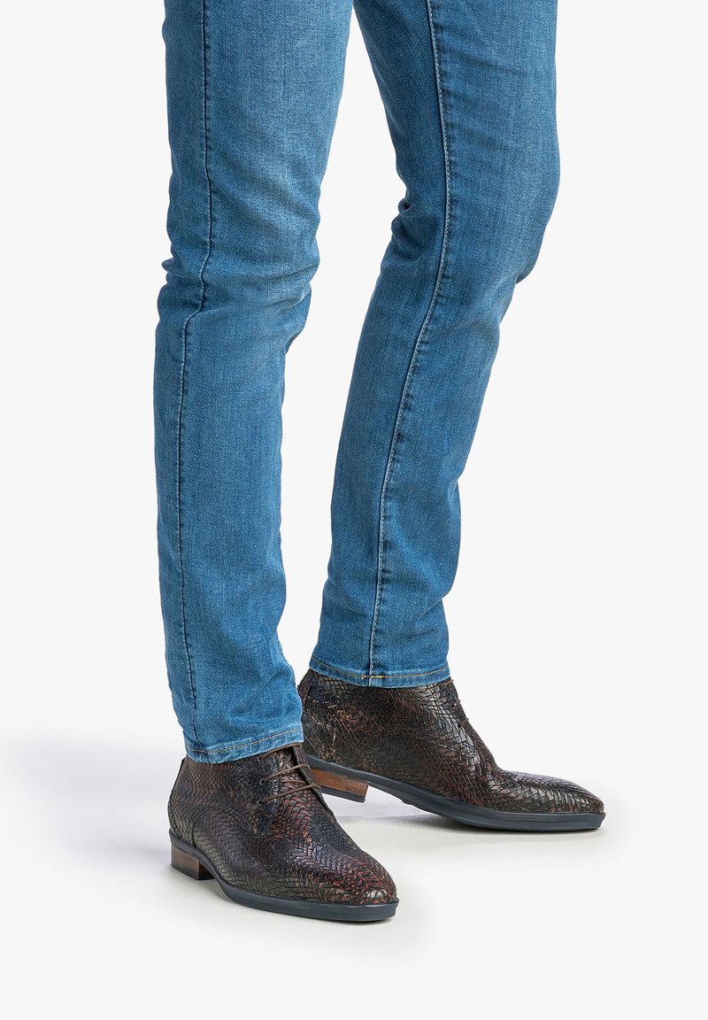 Dunkelbraune Leder-Ankle-Boots mit strukturiertem Muster, schlankem Design und runder Spitze, kombiniert mit eng anliegenden blauen Jeans.