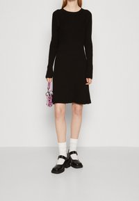 Vestito a maglia nero a coste con maniche lunghe, scollatura tonda e silhouette aderente. Abbinato a scarpe con plateau nere e calzini bianchi alla caviglia.