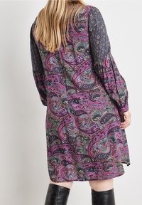 Mönstrad klänning med en flerfärgad paisleymönstring i lila, grönt och svart, med genomskinliga långa ärmar och elastiska manschetter.