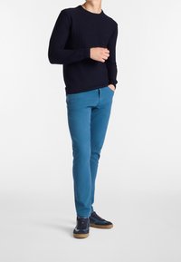 Navy ribbed sweater paired with bright blue slim-fit pants and navy sneakers with brown accents. Simple, casual outfit without patterns.