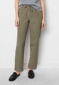 Olijfgroene, recht gesneden broek met een koord in de taille, gemaakt van zachte stof. Geloofd met zwarte instappers, met gestikte details.