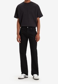 Camiseta negra de algodón con mangas cortas y cuello redondo, combinada con jeans negros de pierna recta y zapatos deportivos grises con rayas negras.