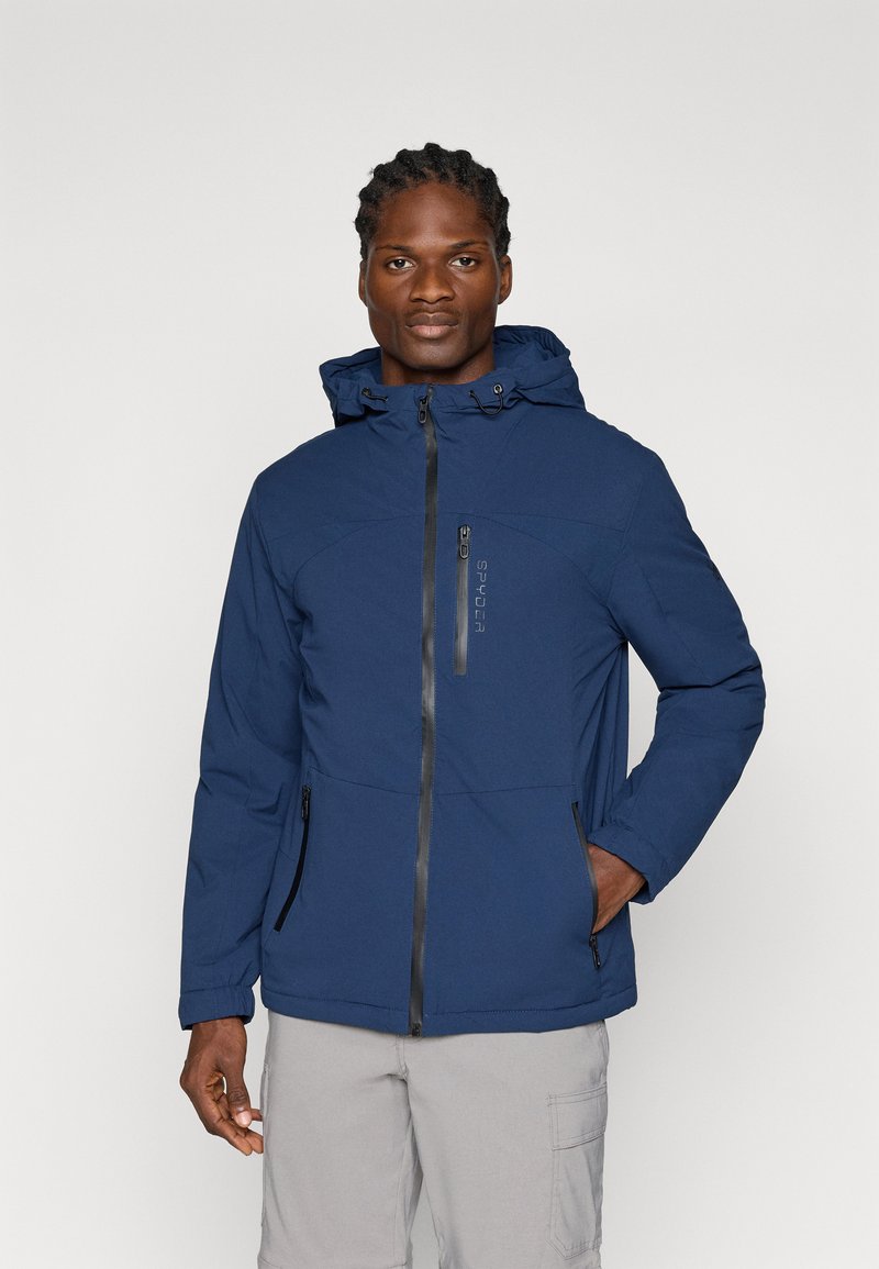 Chaqueta aislante de un color azul marino con capucha, que cuenta con un cierre frontal y dos bolsillos laterales con acentos en negro. Tejido suave y corte holgado.