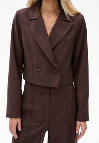 Brązowa skórzana marynarka w kroju krótkim z klapami, podwójnymi guzikami i długimi rękawami. Wykonana z gładkiego materiału o dopasowanym kroju i minimalnych detalach szycia.