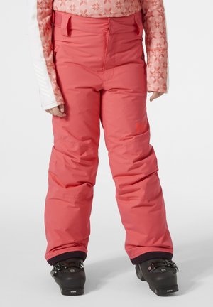 Los pantalones de nieve rosa cuentan con un diseño acolchado, bolsillos de carga, una cinturilla ajustable y puños negros, combinados con botas de esquí negras.