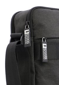 Bolsa de hombro de tela negra con cremalleras, que cuenta con dos tiradores y una correa de hombro resistente. Material texturizado y detalles de construcción robustos evidentes.
