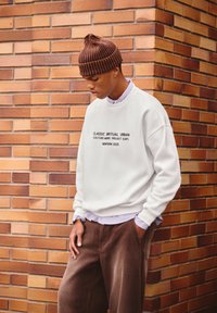 Felpa bianca con testo nero, pantaloni in corduroy marroni e un berretto a righe marroni. Il testo include "CLASSIC RITUAL URBAN" e "NEWYORK 2025."