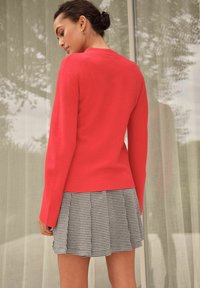 Red knit sweater paired with a black and white houndstooth pleated skirt. The outfit features long sleeves and a fitted silhouette.