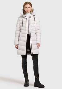 White padded long coat with a hood, featuring thick horizontal stripes, a front zipper, and black accents. Worn over black leggings and boots.