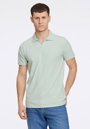Polo shirt verde chiaro con una texture morbida, maniche corte e colletto standard, abbinato a jeans blu. Design semplice, senza motivi.