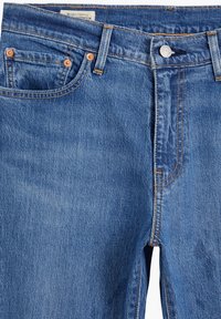 Ljusblå denimjeans med kopparnitar, orange sömmar och en klassisk femficksdesign. Utrustad med knappgylf och rak ben.