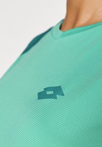 Türkiissin värvi sportlik särk ribatekstuuriga, millel on tume roheline logo rinnal ja kontrastne tume roheline õlavarrepaneel.