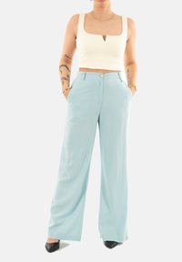 Pantaloni a gamba larga azzurri chiari con una texture liscia, dotati di tasche frontali e chiusura con bottone, abbinati a un top cropped bianco a coste.