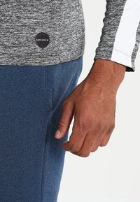 Close-up of a person wearing a grey and white long-sleeve shirt and blue pants, with a visible "BJÖRN BORG" logo on the shirt.