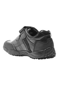 Chaussure de sport noire avec un matériau synthétique lisse, une sangle Velcro, des panneaux latéraux texturés et une semelle robuste avec des motifs de traction.