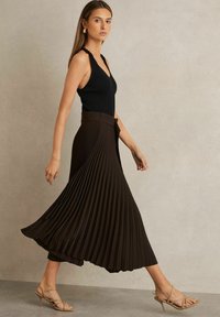 Body nero a coste abbinato a una gonna midi marrone fluida e plissettata. Il modello indossa sandali con tacco a strisce color marrone chiaro. Aspetto liscio e dai materiali texturizzati.