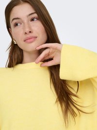 Suéter de punto amarillo claro con cuello alto y mangas largas. Textura suave, ajuste ligeramente holgado y puños acanalados que aportan detalle.