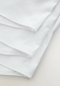 Articoli in tessuto bianco impilati, con una superficie liscia. La parola "Clarks" è ricamata in rilievo nella parte inferiore destra dell'oggetto in cima.
