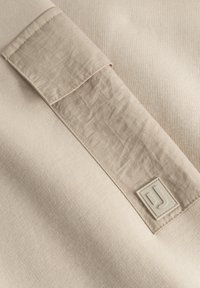 Textil bej cu un model de tricot texturat; prezintă o pată netedă cu un eticheta de logo de culoare deschisă; strălucire subtilă și detalii fine de cusătură.