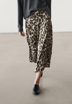 Person walking wearing leopard print wide-leg pants, black loafers, and a dark grey long-sleeve sweater against plain background.