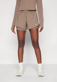 Hnědé sportovní šortky s elastickým pasem, se bílým logem Nike. Nosit s světlými teniskami a bílými krátkými ponožkami.