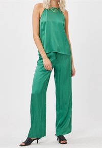 Ensemble composé d'un haut dos nu en satin vert et d'un pantalon à jambes larges. Texture lisse, coupe décontractée, avec une taille à cordon. Porté avec des talons noirs à bout ouvert.