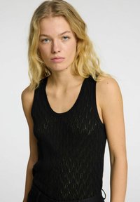 Black knitted tank top featuring a wave pattern, scoop neckline, and sleeveless design. The texture is lightweight and sheer.