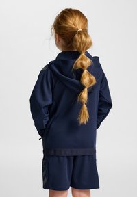 Marinblå sportoutfit med huvad jacka och matchande shorts, texturerat tyg och ljusgrå logodetaljer.